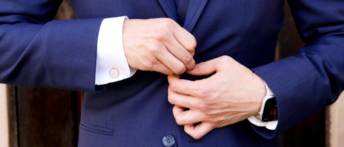 Close-up of a man's hands fastening a navy suit button, showcasing elegance and style.